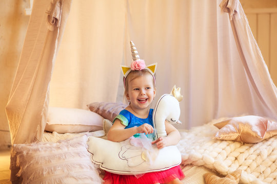 3-4 year old, happy and sympathetic girl sits on a canopy bed and hugs a swan stuffed toy, a birthday in the style of a unicorn