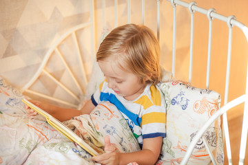 little cute boy blond 4-5 years old reading a book in bed interesting book, day, bedroom, bed