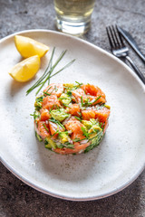 PERUVIAN FOOD. Salmon ceviche with avocado, spring onion and lemon on white plate served with white wine