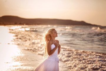 Fototapeta na wymiar beautiful bride in white dress at sunset on the ocean or sea on an exotic island by the water. Sunny horizon. Wedding, honeymoon concept. Young woman resting on vacation in nature