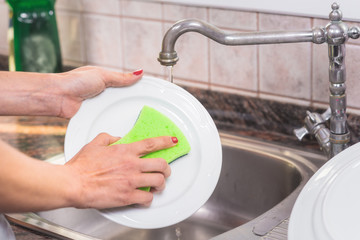 Young woman with red manicure, washing dishes in the sink of the kitchen .