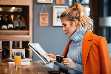 Young businesswoman drinking coffee and reading newspaper in a cafe.