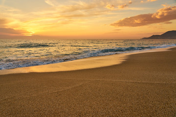 Colorful sunset at the tropical sandy beach, waves with foam hitting sand. Copy space.