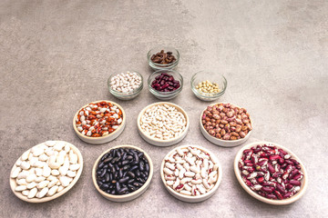 Assortment of beans on a stone background. Crimson cranberry, red, painted pony, black turtle, brown, black-eyed, Jacob's Cattle (heirloom), lima, navy, asparagus bean and soybean.