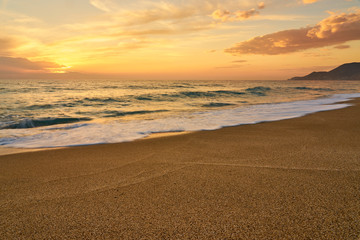 Colorful sunset at the tropical sandy beach, waves with foam hitting sand. Copy space.