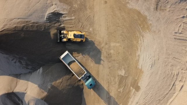 Top aerial time lapse of bulldozer loading stones into empty dump truck in open air quarry.