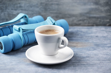 Cup of coffee and dumbbells on blue wooden background. Copy space.