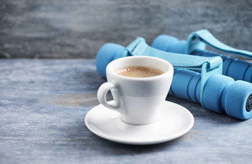 Cup of coffee and dumbbells on blue wooden background. Copy space.