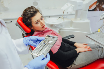 Dental instruments are displayed in the hands of the dentist. Dressed in blue gloves. In a silver medical tray in the dentist's office.