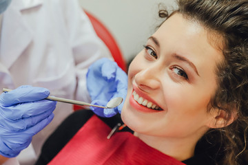 The doctor does professionally. The ugly patient mimics her white teeth, examined by the dentist in the clinic. A doctor is a good woman working in a mask and gloves.