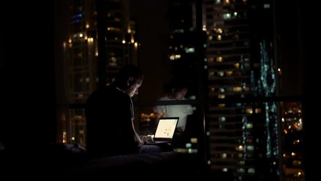 Young man finish working on aptop and falling asleep on bed at night at home, 4K