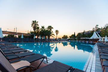 swimming pool with palm trees at sunset. water reflection