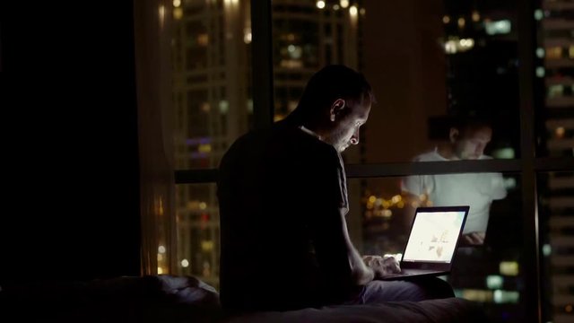 Young man finish working on aptop and falling asleep on bed at night at home
