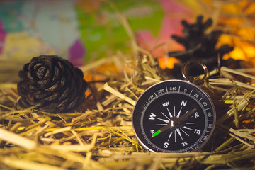 Compass with paper maps and pine flowers placed on dry wheat straw in morning sunlight. Concept of adventure tourism or survival in the forest.