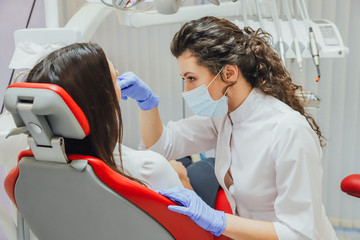 Young woman sitting in a dental chair for appointment of a doctor. During this time, she was very worried about fear, opened her big eyes. A doctor is a good woman in medical clothes, which makes a