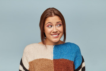 Portrait of young girl in a multi-colored sweater feels guilty anxiously looks to the side, she bit...