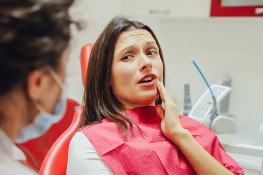 Close-up portrait of a sad young girl with a painful tooth, a doctor in office chairs, an isolated dentist office background clinic.