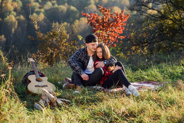 Happy young man hugs his girlfriend tenderness and having rest on picnic in the park. Couple in love having rest at sunset.