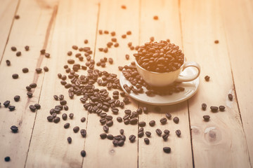 White cup full of coffee beans on Roasted Coffee Beans and wooden table in nature background