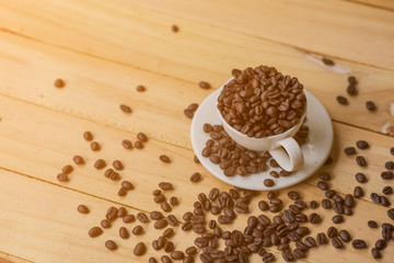 White cup full of coffee beans on Roasted Coffee Beans and wood background, top view
