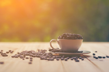 White cup full of coffee beans on Roasted Coffee Beans and wooden table in nature background