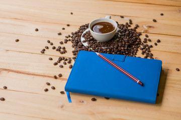 Cup of coffee white notebook, pen, coffee beans and alarm clock on a Desktop from wooden plank. Top view.