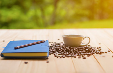 White cup full of coffee beans on Roasted Coffee Beans and wooden table in nature background