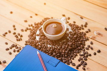 Cup of coffee white notebook, pencil, coffee beans on a Desktop from wooden plank. Top view.