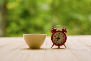 White alarm clock with red coffee cup on wooden table with morning light, Start up concept