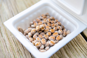 Closeup of frozen Asian Japanese natto fermented soy dish meal in styrofoam container Japan box on wooden table macro