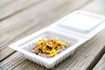 Closeup of Asian Japanese natto fermented soy dish meal in styrofoam container Japan box and toppings soy sauce garlic and ginger on wooden table macro