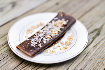 Closeup of chocolate vegan crepe dessert wrap with rice crisps and coconut flakes made in dehydrator with bananas on plate wooden table
