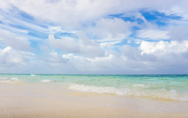 Sunny tropical beach with blue sky and scattered white clouds and clear water