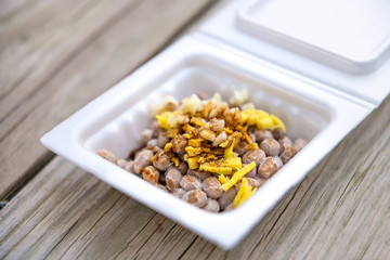 Asian Japanese natto fermented soy dish meal closeup in container Japan box and toppings soy sauce garlic and ginger on wooden table macro