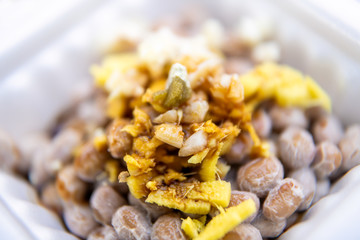 Macro closeup of Asian Japanese natto fermented soy dish meal in styrofoam container Japan box and toppings soy sauce garlic and ginger