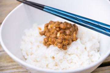 Closeup of blue chopsticks on Asian Japanese natto fermented soy dish meal sticky slimy texture in plain white steamed rice in bowl