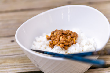 Blue chopsticks closeup on Asian Japanese natto fermented soy dish meal sticky slimy texture in plain white steamed rice in bowl