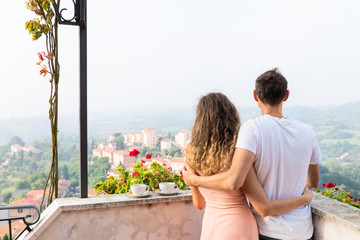 Woman and man romantic couple on terrace garden outside in Italy with mountain view of Chiusi cityscape Umbria near Tuscany and tea or coffee cups in breakfast morning with fog mist