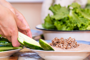 Table with hands setting of healthy vegan vegetarian lunch or dinner green vegetables cucumbers salad and traditional Russian or Ukrainian buckwheat porridge