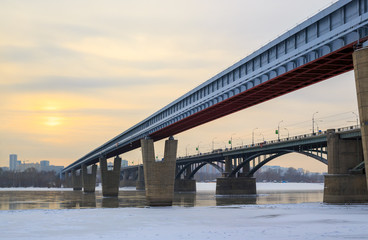 Fototapeta na wymiar View of the Metro Bridge and the October Bridge over the Ob River. Novosibirsk, Siberia, Russia. Cold weather. The water is partially covered with ice. In the distance buildings. Place for text.