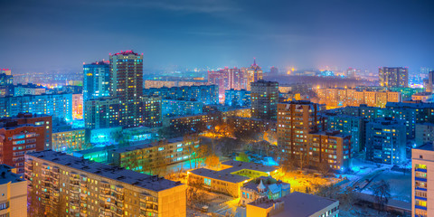 Fototapeta premium Urban panorama. Beautiful top view of the city. Colorful street lighting of the night metropolis. Many high-rise buildings. Cold winter weather. Novosibirsk, Siberia, Russia.