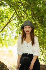 Women white skin lovely brown hair wearing a gray hat red lip wear white shirt wearing black pants women sit poses photography portrait under the tree In the garden.