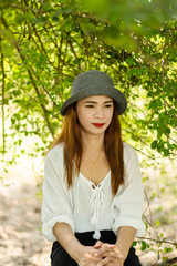 Women white skin lovely brown hair wearing a gray hat red lip wear white shirt wearing black pants women sit poses photography portrait under the tree In the garden.