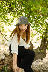 Women white skin lovely brown hair wearing a gray hat red lip wear white shirt wearing black pants women sit poses photography portrait under the tree In the garden.
