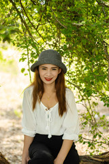 Women white skin lovely brown hair wearing a gray hat red lip wear white shirt wearing black pants women sit poses photography portrait under the tree In the garden.