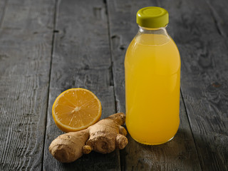 Glass bottle with a drink of ginger root, lemon, orange, honey and cinnamon on a dark rustic table.