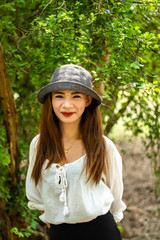Women white skin lovely brown hair wearing a gray hat red lip wear white shirt wearing black pants women standing poses photography portrait under the tree In the garden.