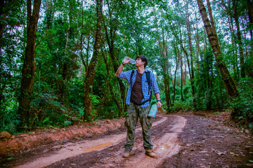 Obraz premium Happy hipster man tourist with backpack drinking water while hiking in nature forest.