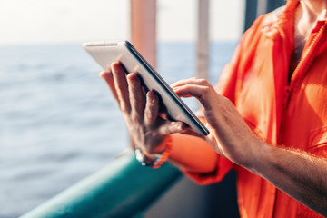 Marine chief officer or captain on deck of vessel or ship watching digital tablet. Internet and...