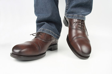 Male legs in jeans and brown classic shoes on white background